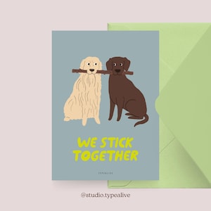 May include: Greeting card with a light blue background featuring two cartoon dogs, one cream-colored and one brown, sharing a stick. The text "WE STICK TOGETHER" is in yellow. A green envelope is visible.