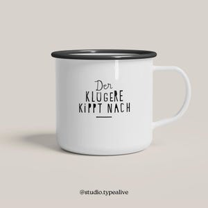 May include: White enamel mug with a black rim and handle. The mug has black text that reads "Der Klügere kippt nach" with a line underneath the text. The text is in German.