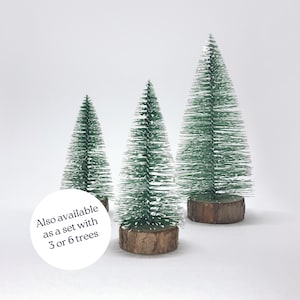 May include: Three miniature artificial Christmas trees with green flocked needles and brown wooden bases. Also available as a set with 3 or 6 trees.