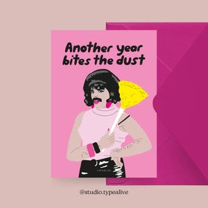 May include: A pink greeting card with the text "Another year bites the dust" features an illustration of a person with a mustache and a yellow duster. The card is accompanied by a pink envelope. The artist's name, "TYPEALIVE", is at the bottom.