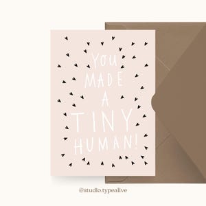May include: A pink card with black hearts scattered around the text "You made a tiny human!"  The card is on a brown envelope.
