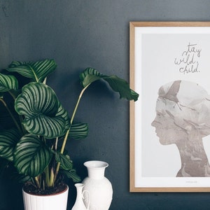 Pu&ograve; includere: Una stampa incorniciata con sfondo bianco e una silhouette di una testa di donna su cui &egrave; sovrapposta una stormo di uccelli. Il testo "stay wild child." &egrave; scritto in corsivo sopra la silhouette.