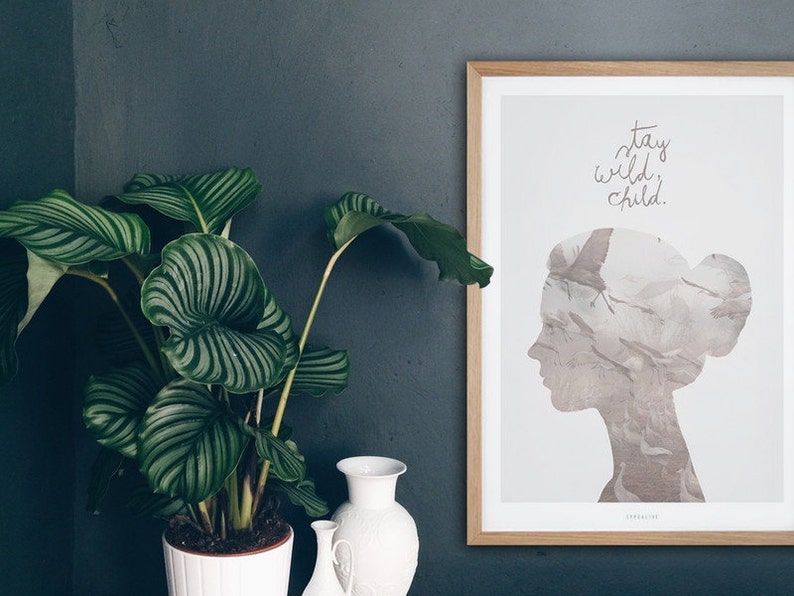 Pu&ograve; includere: Una stampa incorniciata con sfondo bianco e una silhouette di una testa di donna su cui &egrave; sovrapposta una stormo di uccelli. Il testo "stay wild child." &egrave; scritto in corsivo sopra la silhouette.
