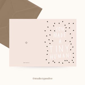 May include: A pink card with black hearts surrounding the text "You made a tiny human!" in white. The card is a new baby announcement.