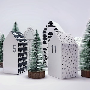 May include: Black and white geometric patterned paper houses with numbers 5 and 11, arranged in a row with small artificial pine trees in front of them.