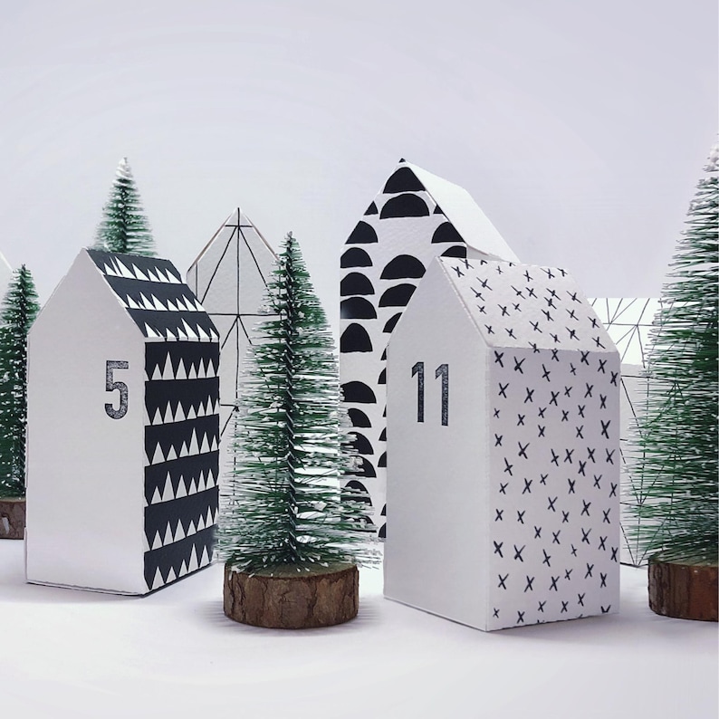 May include: Black and white geometric patterned paper houses with numbers 5 and 11, arranged in a row with small artificial pine trees in front of them.