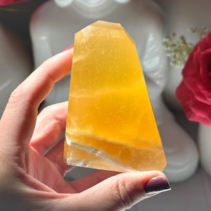 May include: A large, translucent, yellow calcite crystal with white veins. The crystal is shaped like a pyramid and has a smooth, polished surface.