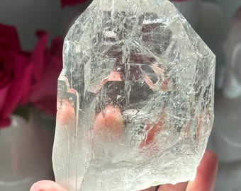 May include: A large, clear quartz crystal with a pointed top and a flat base. The crystal is translucent and has a slightly cloudy appearance. It is a natural crystal and has a rough, uneven surface.