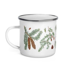 May include: White enamel mug featuring a green and brown pine tree design. The mug has a silver rim and handle.