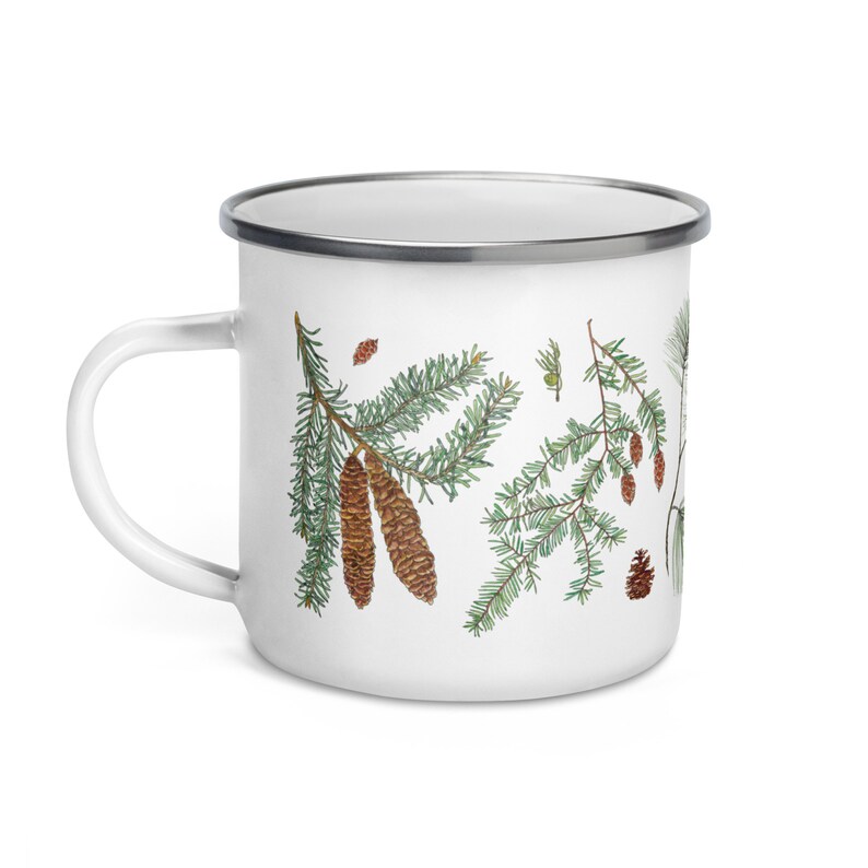 May include: White enamel mug featuring a green and brown pine tree design. The mug has a silver rim and handle.