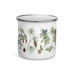 May include: White enamel mug featuring a design of pine branches, pine cones, and juniper berries. The design is in shades of green, brown, and blue.