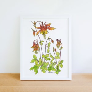 May include: A framed watercolor print of columbine flowers. The artwork features orange and yellow blossoms with green foliage and stems. The white frame sits on a wooden surface against a white wall.