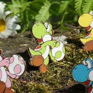 May include: Six colourful Yoshi character enamel pins, each holding a white egg with a different coloured spot. The pins are arranged on a mossy tree trunk.