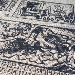 May include: A close-up of a burlap fabric with black ink printed designs. The designs are intricate and feature various patterns, including a dragon-like creature, a figure holding a sword, and a series of symbols. The fabric has a rough texture and a natural brown color.
