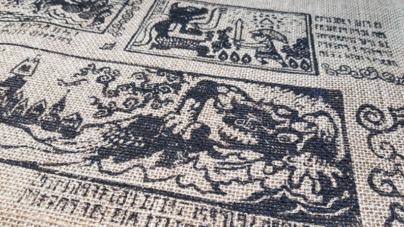 May include: A close-up of a burlap fabric with black ink printed designs. The designs are intricate and feature various patterns, including a dragon-like creature, a figure holding a sword, and a series of symbols. The fabric has a rough texture and a natural brown color.