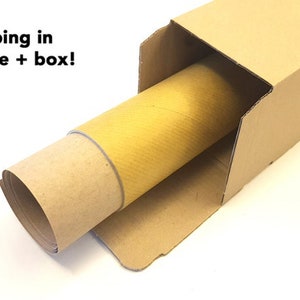 May include: A rolled-up item inside a cardboard tube, placed within a brown cardboard box. The text "Safe shipping in paper tube + box!" is visible in the image. The tube is yellow and the box is brown.