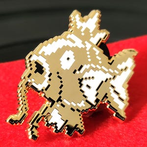 May include: A gold-coloured, pixelated pin depicting a creature with a long, segmented appendage. The pin has white accents and is set against a red background. The pin is likely a collectible item or accessory.