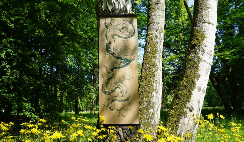 May include: A long, rectangular artwork with a teal illustration of a winding, tree-like form is displayed on a tree trunk. The artwork is on a tan background and is framed by a black bar at the top. The scene is set in a lush green forest.