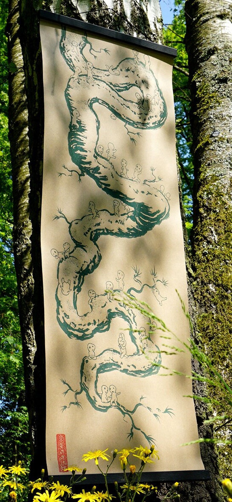 May include: A long, vertical scroll featuring a teal illustration of a winding tree-like form with small figures. The artwork is printed on a tan background and hangs against a tree trunk. The scroll is framed with a black bar at the top.