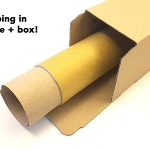 K&ouml;nnte beinhalten: Ein aufgerolltes Poster in einer Pappr&ouml;hre, platziert in einem braunen Pappkarton. Der Text "Safe shipping in paper tube + box!" ist oben links sichtbar.