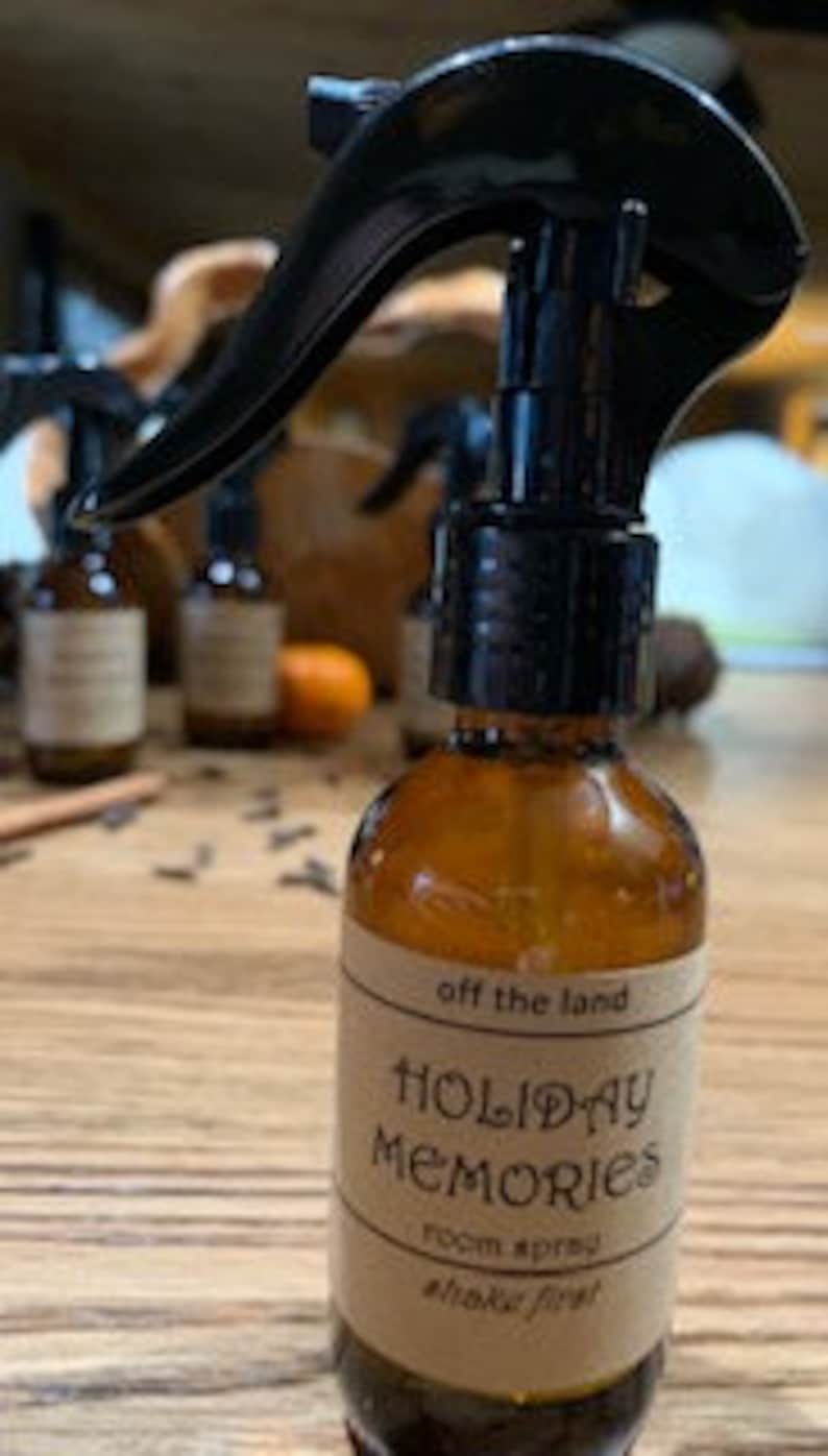 May include: A brown glass bottle with a black spray nozzle filled with room spray. The label reads "off the land HOLIDAY MEMORIES room spray #holidayfirst"