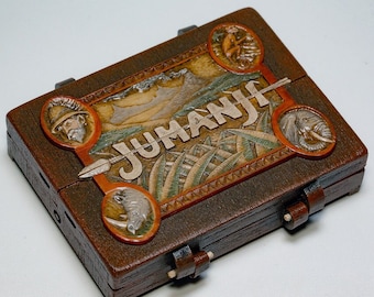 May include: A wooden box game with the word "JUMANJI" on the front. The box is decorated with images of a jungle scene, a rhinoceros, an elephant, and a man with a beard.