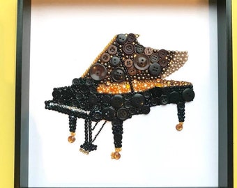 Può includere: Opera d'arte incorniciata raffigurante un pianoforte a coda, realizzato con bottoni marroni e neri di varie dimensioni, con dettagli dorati. L'opera è presentata su uno sfondo bianco, all'interno di una cornice nera.
