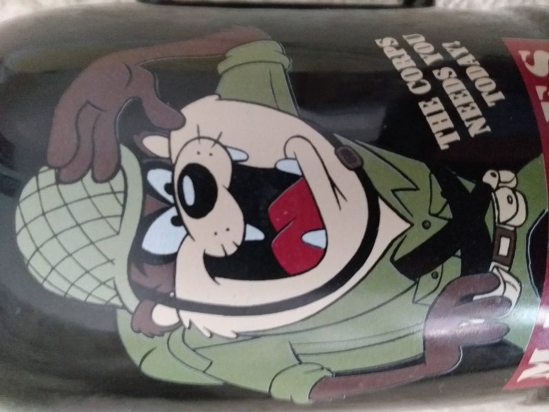 May include: A black and green mug featuring a cartoon character in a military hat and uniform. The text on the mug reads "The Corps Needs You Today".