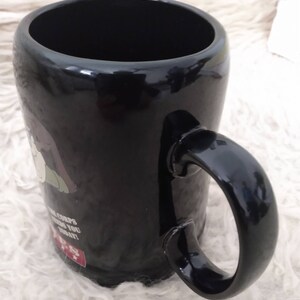 May include: Black ceramic mug featuring a cartoon image of a person wearing a green hat and the text "The Corps needs you today!"