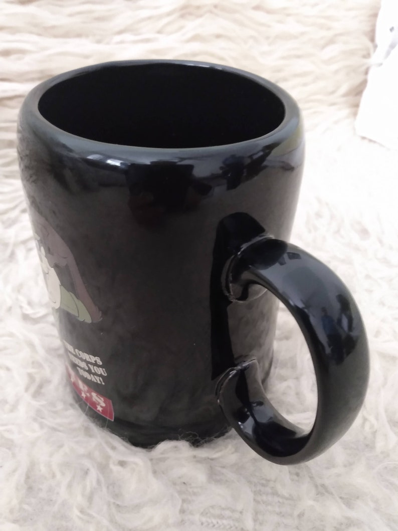 May include: Black ceramic mug featuring a cartoon image of a person wearing a green hat and the text "The Corps needs you today!"