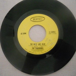 May include: A yellow vinyl record with black text that reads "45 RPM", "EPIC", "5-10094", "ZSP 116386", "THE NAZZ ARE BLUE", "THE YARDBIRDS", and "EPIC MARCAS REGTM PRINTED IN USA".