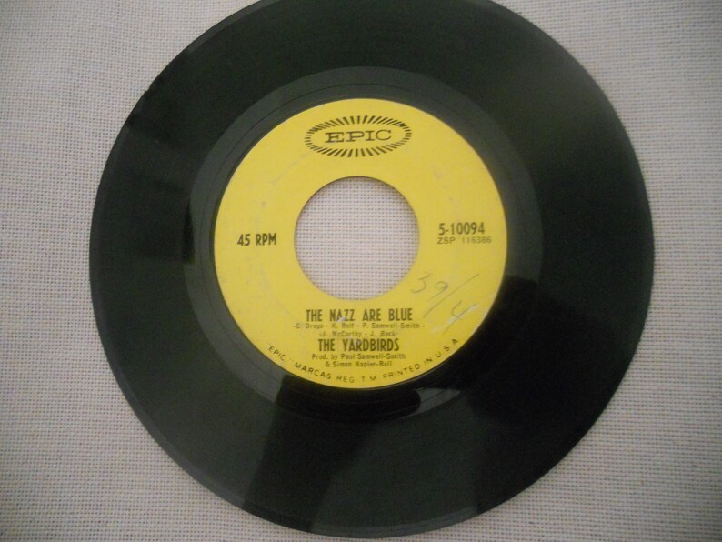 May include: A yellow vinyl record with black text that reads "45 RPM", "EPIC", "5-10094", "ZSP 116386", "THE NAZZ ARE BLUE", "THE YARDBIRDS", and "EPIC MARCAS REGTM PRINTED IN USA".