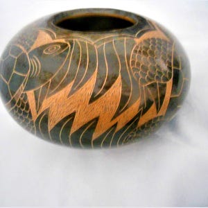 May include: A dark green ceramic bowl with a brown glaze. The bowl is decorated with a carved design of fish and seaweed.
