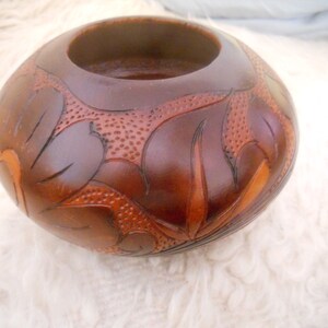 May include: A brown wooden bowl with a carved floral design. The bowl has a wide opening and a rounded bottom.
