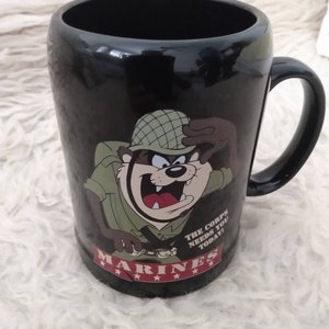 May include: Black ceramic mug featuring a cartoon image of a Tasmanian Devil dressed as a Marine. The mug has the text "The Corps Needs You Today!" and "Marines" with five stars below the text.