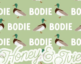 May include: A green background with a repeating pattern of ducks and the word "BODIE". The text "Honey & Trie" is in a white circle in the center of the image.