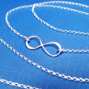 May include: A silver infinity symbol necklace on a blue background. The necklace is made of a delicate chain.