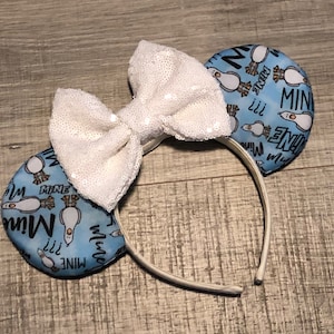 May include: White sequined bow headband with blue fabric ears featuring a cartoon penguin and the text "Mine" repeated.