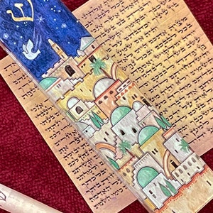 May include: A mezuzah with a colorful illustration of a cityscape with a star and a dove. The mezuzah is attached to a scroll of Hebrew text.