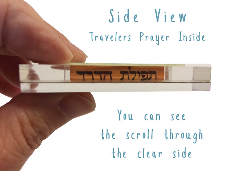 Peut inclure: Un &eacute;tui en acrylique transparent contenant un petit rouleau. Le rouleau est visible &agrave; travers l'&eacute;tui transparent. Le texte "תפילת" est visible sur le rouleau. Le texte "Travelers Prayer Inside" est &eacute;crit en bleu sur un fond blanc au-dessus de l'&eacute;tui.