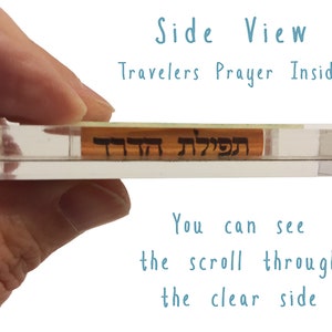 Puede incluir: Una caja de acr&iacute;lico transparente con un peque&ntilde;o rollo en su interior. El rollo es visible a trav&eacute;s de la caja transparente. El texto "תפילת" es visible en el rollo. El texto "Travelers Prayer Inside" est&aacute; escrito en azul sobre un fondo blanco.