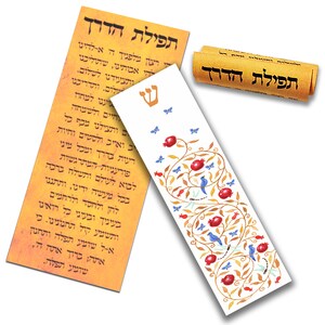 Puede incluir: Un marcap&aacute;ginas blanco con un dise&ntilde;o de &aacute;rbol de granada dorado y rojo. El marcap&aacute;ginas est&aacute; decorado con p&aacute;jaros azules, mariposas y lib&eacute;lulas. El texto "תפילת הדרך" est&aacute; escrito en hebreo en un rollo enrollado en el fondo.