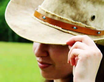 May include: A woman wearing a brown cowboy hat with turquoise accents and three leather bracelets with turquoise accents on her wrist.