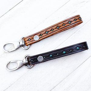 May include: Two leather keychains with a silver swivel clasp. One keychain is brown with turquoise accents and the other is black with turquoise accents.