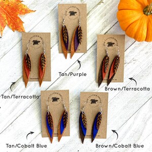 May include: Four pairs of leather earrings with a feather design. The earrings are layered with two different colors of leather. The colors are tan and purple, tan and terracotta, tan and cobalt blue, and brown and cobalt blue.