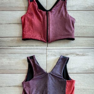 Puede incluir: Dos vistas diferentes de un sujetador deportivo rojo y morado con tirantes negros y una cremallera en la espalda. El sujetador tiene una tela texturizada.