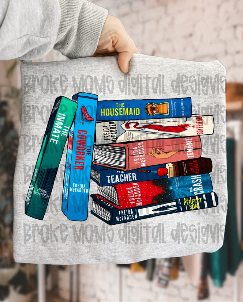 May include: A gray sweatshirt featuring a stack of books with titles like "The Housemaid" and "The Coworker." The books have colorful covers and the author's name, Freida McFadden, is visible. The words "Broke Moms digital designs" are printed on the sweatshirt.