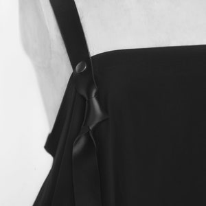 Puede incluir: Vestido negro de hombros descubiertos con un detalle de correa de cuero y un lazo en el escote.