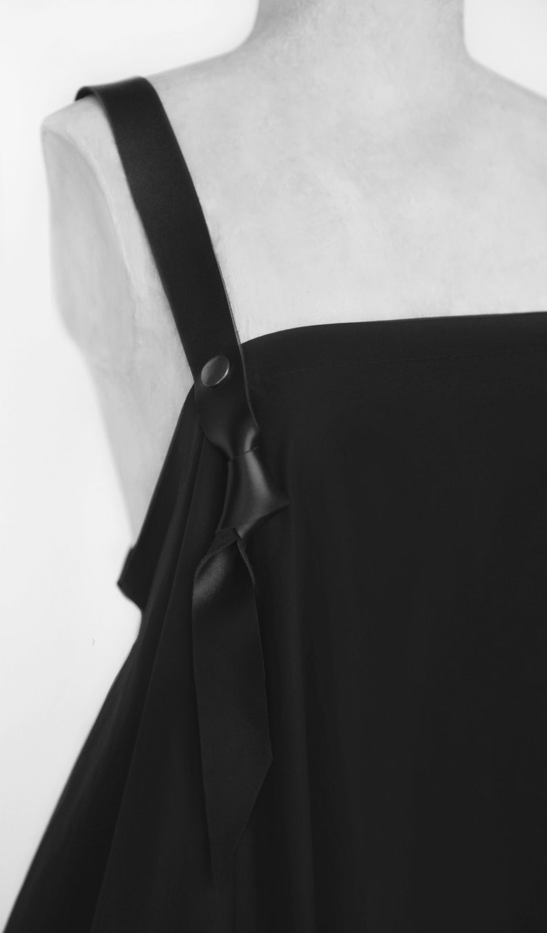 Puede incluir: Vestido negro de hombros descubiertos con un detalle de correa de cuero y un lazo en el escote.