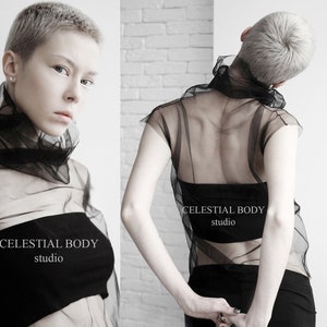 May include: A black sheer top with a high neck and short sleeves. The top is made of a lightweight, flowing fabric. The model is wearing the top with a black bandeau underneath. The text "CELESTIAL BODY studio" is printed on the front of the top.
